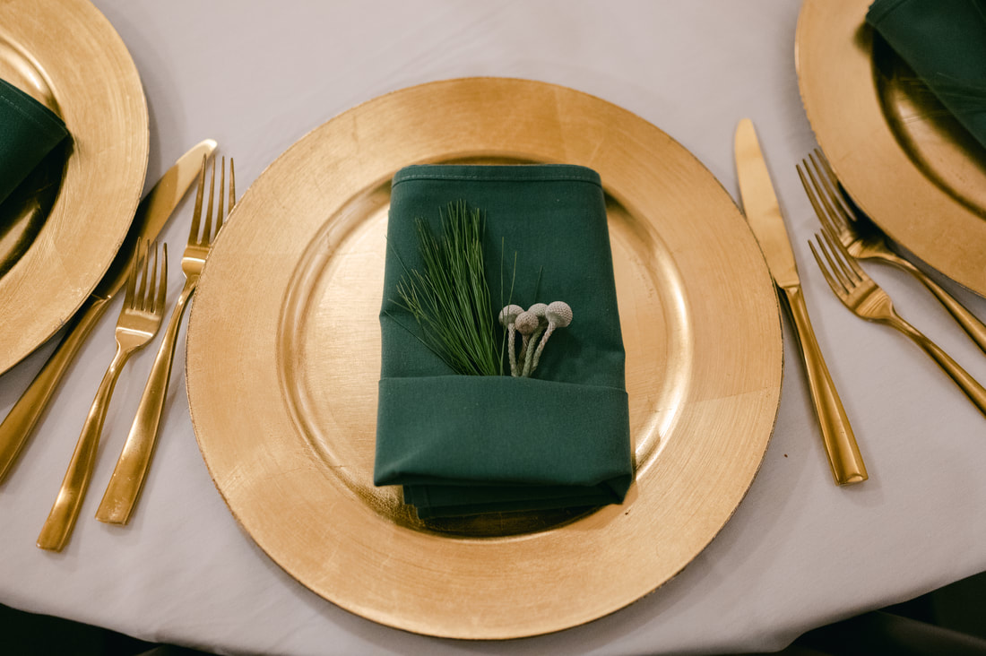 Gold charger plate and gold flatware with emerald napkin and winter green sprigs
