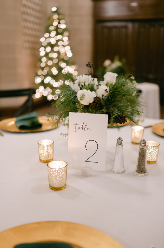 Evergreen and white flower centerpiece with gold votive candles and table number