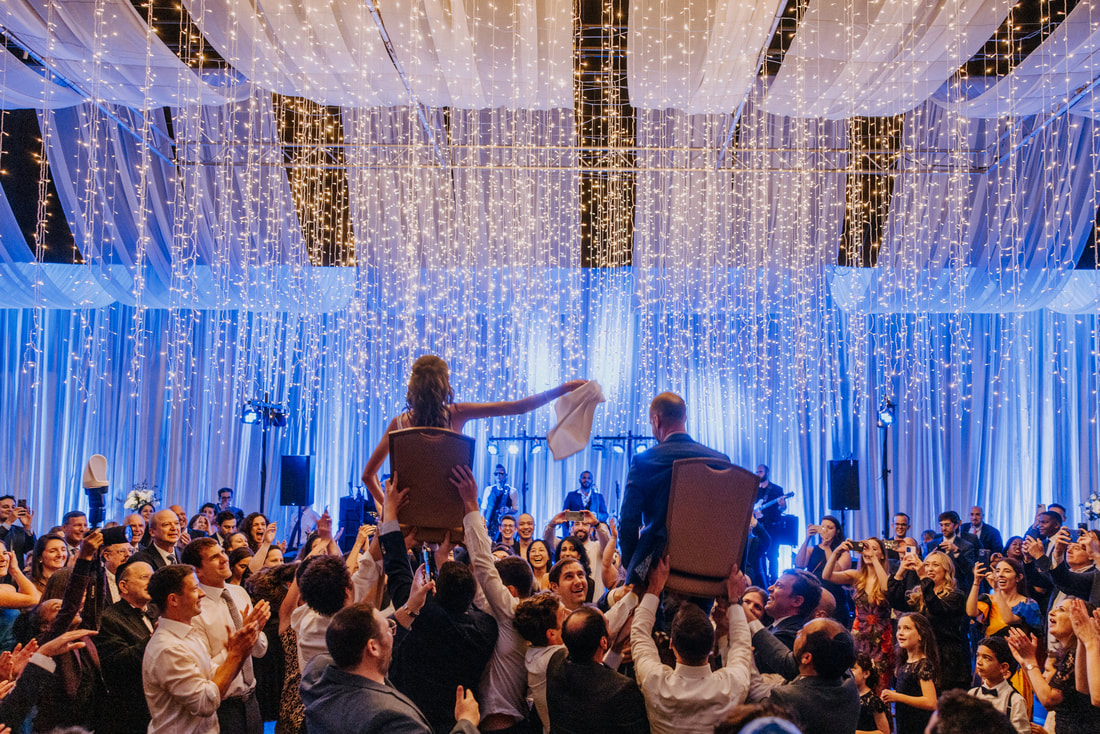 Hora dancing under string lights with draping and blue uplighting